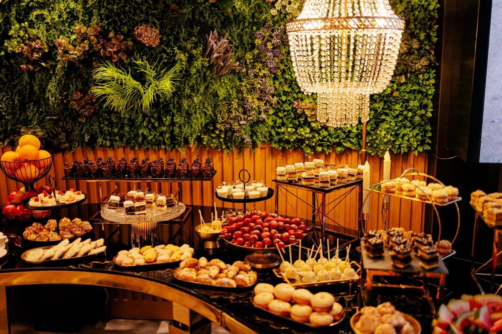Candy Bar cu prăjituri, sub un perete de flori și candelabre